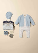 Flat lay of baby gift set with pale blue cardigan, cloud print bodysuits, knit hat, booties and socks