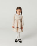 Front view full body of toddler girl with braided pigtails wearing sand striped dress with white collar, black mary jane shoes and white tights, studio background