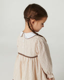 Close up side profile of toddler girl with braided pigtail looking downward, wearing sand striped dress with white collar and brown lace trim visible at shoulder, studio background