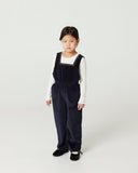 Girl in navy corduroy overalls and cream top laughing, side view against plain background