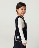 Toddler girl in navy corduroy overalls with embroidered sun pocket, side profile against plain background