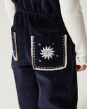 Close up of navy corduroy overalls back pocket embroidered with a sun face and stars in cream and pink thread