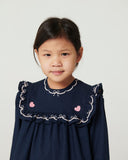 Studio portrait of a girl wearing a navy dress with an embroidered ruffled collar