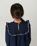 Back view of a navy dress with a ruffled collar edged in bow embroidery