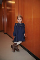 Girl in a navy embroidered dress with cowboy boots in a wood paneled hallway