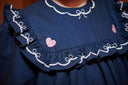 Close up detail of a navy dress ruffled collar with bow embroidery and pink heart appliques