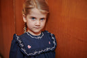 Close up of a navy dress with a ruffled collar embroidered in bows and pink heart appliques