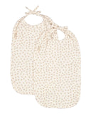 Two cream-colored cotton baby bibs with a small beige floral pattern, featuring tie-neck straps and a small fabric brand tag.
