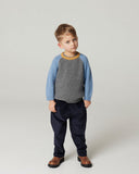 Toddler boy wearing grey and blue color block ribbed knit sweater with navy corduroy pants and brown boots, studio background