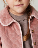 Close up of girl wearing pink quilted jacket with scalloped collar over brown ribbed knit dress, braided hair