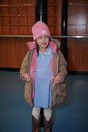 Girl wearing light blue ribbed knit dress and pink beanie, opening tan puffer coat with pink fleece lining, cowboy boots