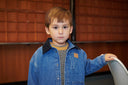 Close up of boy wearing denim jacket with navy corduroy collar over mustard sweater, wood paneled background