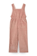 Girl wearing pink corduroy overalls over cream top with black mary jane shoes, standing in studio