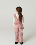 Close up of girl wearing pink corduroy overalls with lace trimmed square neckline over cream top, studio portrait