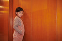 Two girls holding hands in wood paneled hallway, one in pink corduroy overalls with brown cowboy boots, one in pink striped dress with white tights