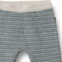 Close-up of a knit baby tights or leggings with a textured pattern of light blue, gray, and black, featuring a ribbed cream waistband.