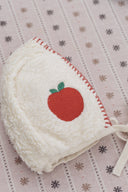Cream sherpa apple bonnet with red embroidered apple and green leaves, close up flat lay