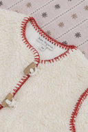 Close up of cream sherpa coat collar and wooden toggle closure with red blanket stitch trim, on snowflake print backdrop