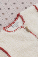 Close up of cream sherpa coat neckline, Bebe Organic size label and red blanket stitch trim, on snowflake print backdrop