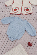 Cream sherpa coat with red apple applique pockets and blanket stitch trim, styled flat lay with a light blue corduroy romper and felt heart on snowflake print