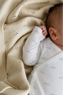 Close up of baby arm in pale blue cloud print sleeve, resting on cream knit blanket