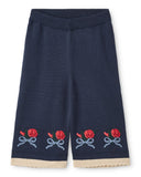Navy blue pants with embroidered red roses and beige trim on a white background