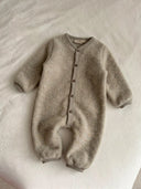 A baby's long-sleeve, one-piece fleece sleeper in a soft taupe-beige color, laid flat on a white textured blanket. The sleeper features a button-down front and ribbed cuffs and hem.