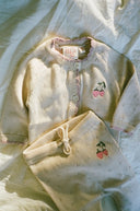 Cream knit cardigan and pants set with strawberry embroidery and pink trim, flat lay on bedding