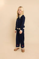 Child wearing navy knit cardigan and matching pants with red rose embroidery near hem, side profile studio shot
