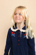 Child wearing navy knit dress with cream collar and red rose embroidery, close up portrait
