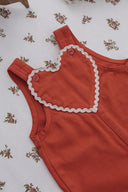 Close up of overall heart bib detail, rust red fabric with cream ric rac trim and matching buttons