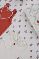 Rust red overall and cream apple embroidered footed romper flat lay, styled with an apple patchwork blanket