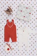 Rust red overall, cream footed romper with apple embroidery, apple patchwork blanket, and apple bonnet, flat lay with a wooden toy horse