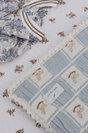 Close up of blue rocking horse patchwork blanket beside a blue floral baby garment