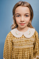 Close up portrait of girl wearing check dress showing smocked bodice and cream collar embroidered with pink roses