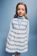 Close up studio portrait of girl in cream apron dress with blue floral stripe print and light blue turtleneck, soft smile