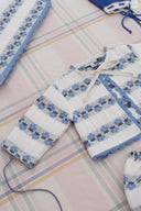 Close up of cream cardigan sleeve and collar with blue floral stripe pattern, matching blue bonnet in corner, on plaid fabric