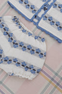 Close up of cream bloomers with blue floral stripe pattern, matching blanket corner visible, on plaid fabric