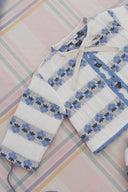 Close up of cream cardigan tie closure and scalloped trim with blue floral stripe pattern, on plaid fabric