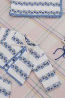 Close up of cream cardigan with tie bow closure, blue floral stripe pattern, matching blanket corner visible, on plaid fabric