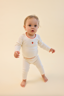 Baby standing wearing cream pointelle leggings and matching bodysuit with strawberry embroidery
