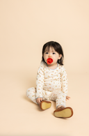 Baby sitting wearing cream pajama set with soft pink poppy print, studio portrait with pacifier