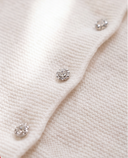 Macro detail of a crystal jeweled button on off white cashmere cardigan knit