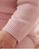 Close up of ribbed cuff on light pink cashmere romper sleeve, baby wrist resting on cherry print bedding