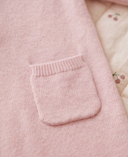 Close up of patch pocket on light pink cashmere romper, baby lying on cherry print quilted bedding