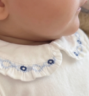 Close up of ruffled collar with blue floral smocking embroidery on ivory bodysuit