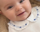 Baby smiling wearing ivory bodysuit with ruffled collar and blue floral smocking