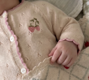 Close up of soft white knit cardigan with strawberry embroidery and pink scalloped trim on sleeping baby