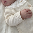 Close up of newborn hand resting on pearl cashmere cotton cardigan button placket with scalloped trim