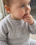 Close up of baby wearing light grey cashmere sweater with fair isle knit pattern at the chest, hand near mouth
